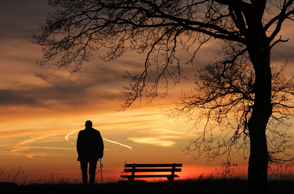 Alter Mann bei einer Parkbank, welcher den Sonnenuntergang schaut. Er überlegt ob er seine Immobilie verkaufen soll.